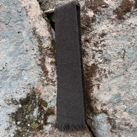 Tummanharmaa kapea villahuivi roikkumassa kaliota vasten.