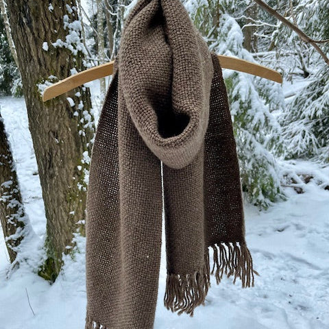 Kapea ruskea villahuivi roikkumassa kuten kaulassa. Taustalla luminen metsä.