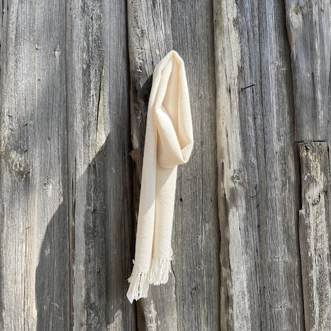 Käsinkudottu luonnonvalkoinen villahuivi roikkumassa ladon seinällä