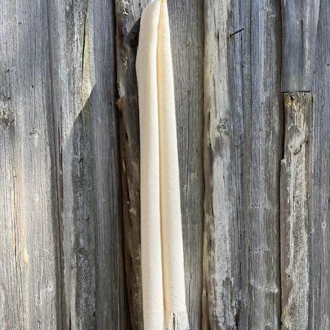 Käsinkudottu luonnonvalkoinen villahuivi roikkumassa suorana ladon seinällä