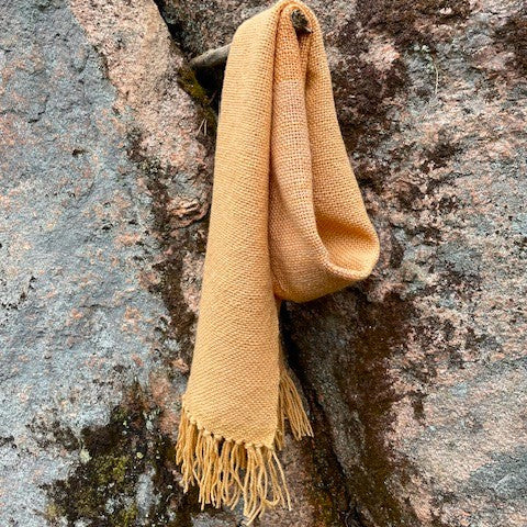 Vaalea oranssi villahuivi roikkuu kuten kaulassa. Taustalla kallio.