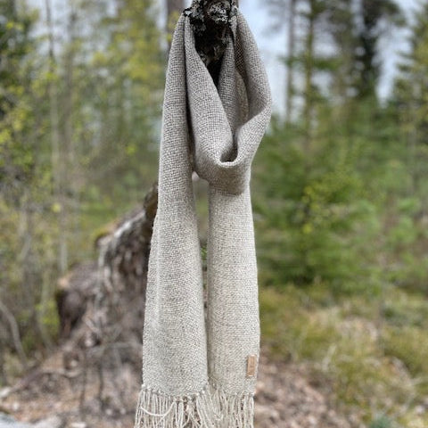 Vaaleanharmaa villashaali roikkumassa kuten kaulassa, metsäinen maisema taustalla.