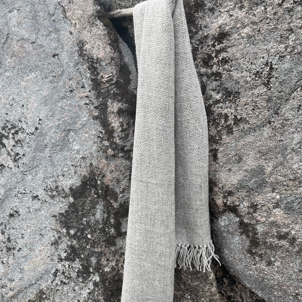 Vaaleanharmaa villashaali roikkumassa kuten kaulassa kalliota vasten.