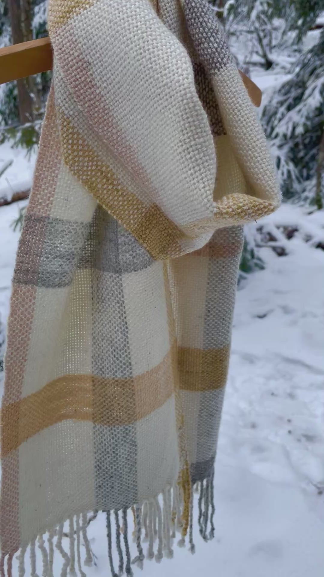 Käsinkudottu kolmivärinen villahuivi heiluu tuulessa henkariin ripustettuna